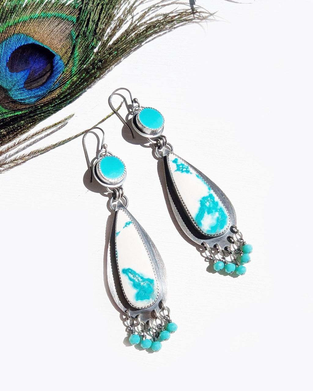 Turquoise and silver earrings with a peacock feather on a white background