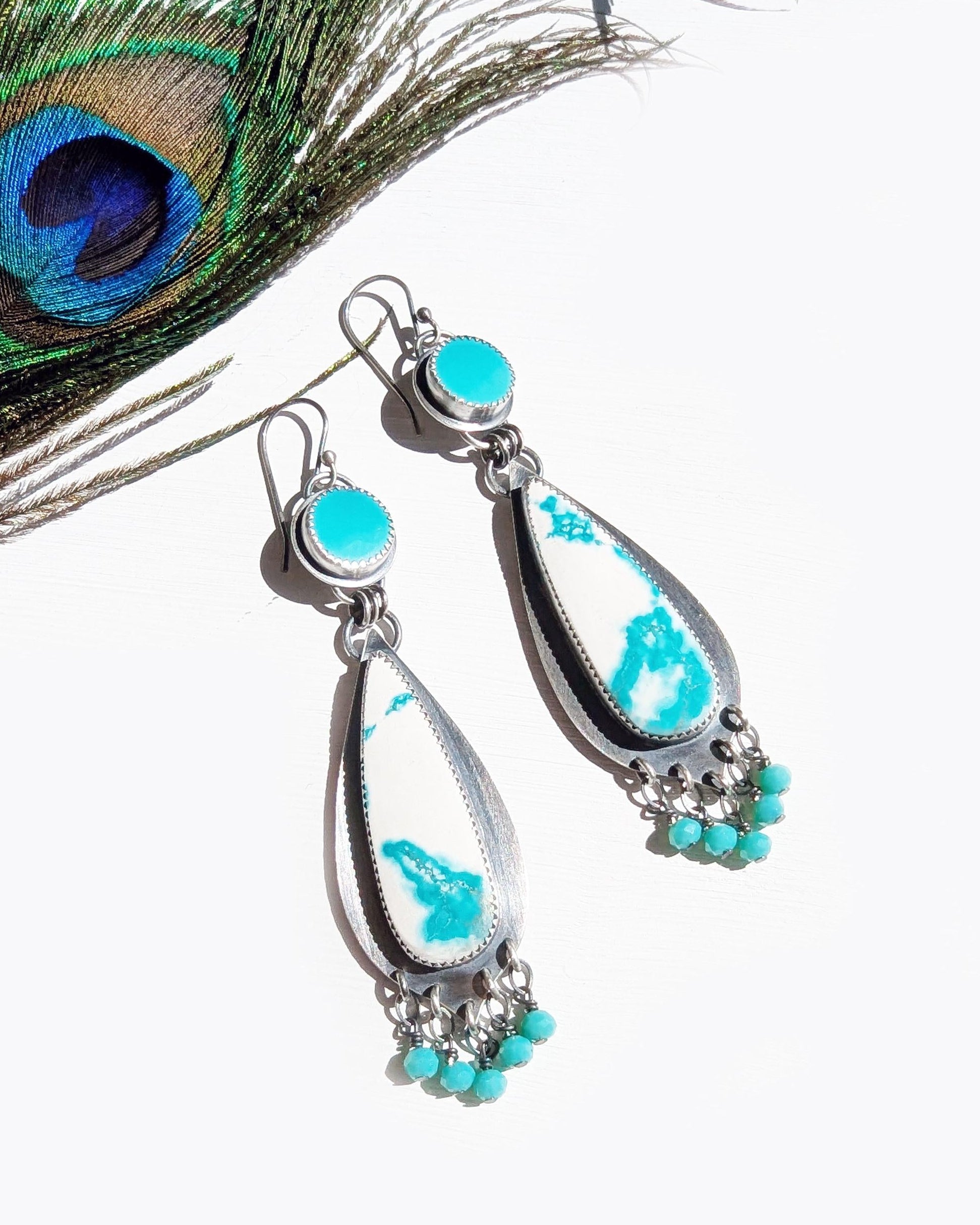 Turquoise and silver earrings with a peacock feather on a white background