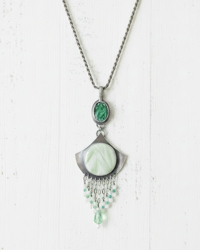 Necklace with green gemstones and silver pendant on a white background.