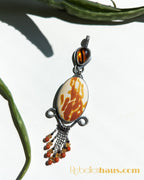 Decorative pendant with a central orange and red stone and hanging beads against a white background.