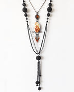 Layered necklace with black beads and a central pendant on a white background