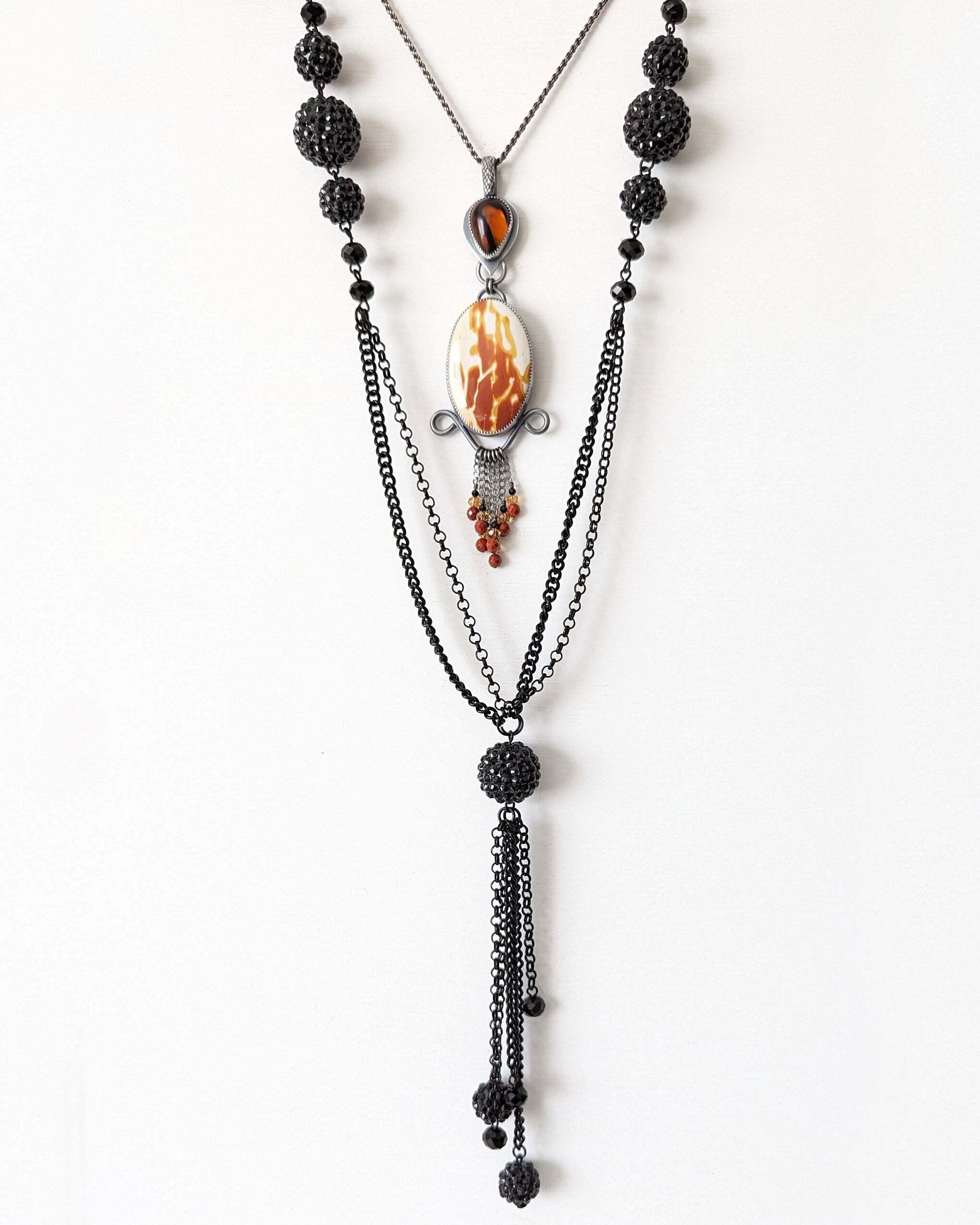 Layered necklace with black beads and a central pendant on a white background