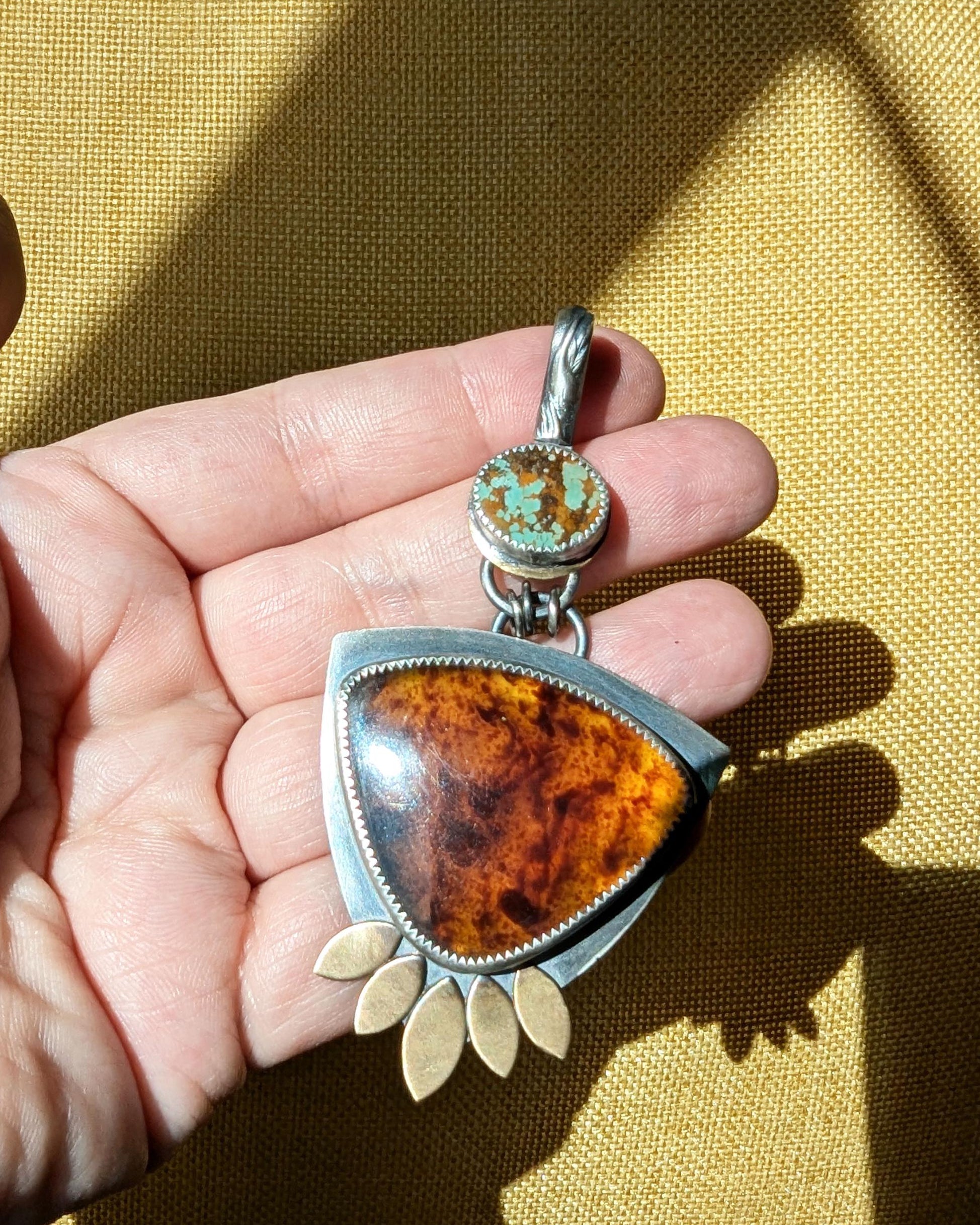Boho luxe pendant featuring stabilized turquoise and glowing amber in bright sunlight