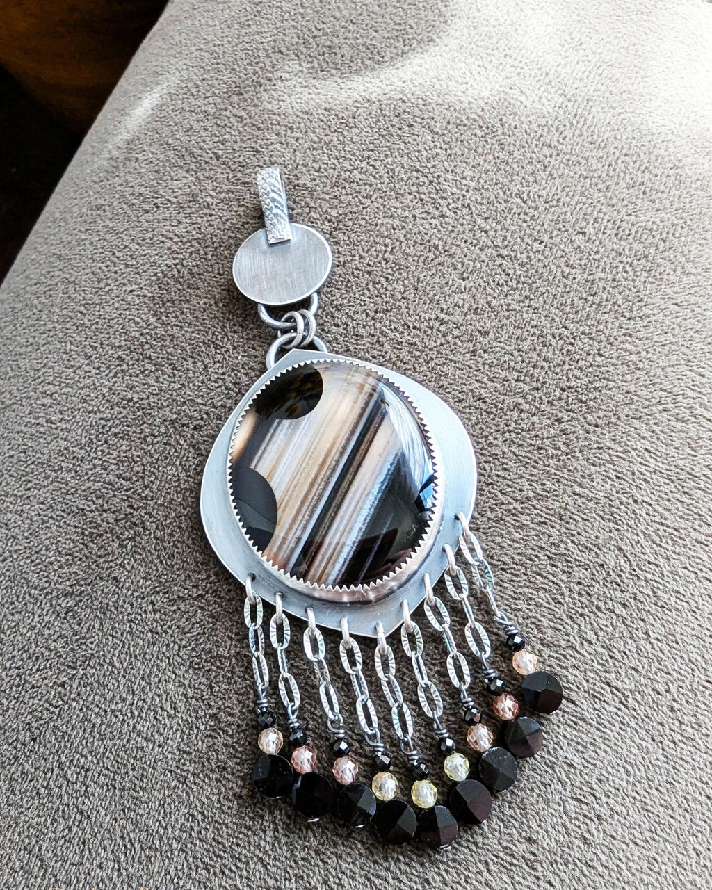 Close up of banded gemstone pendant with black onyx, gold zircon, and black spinel fringe