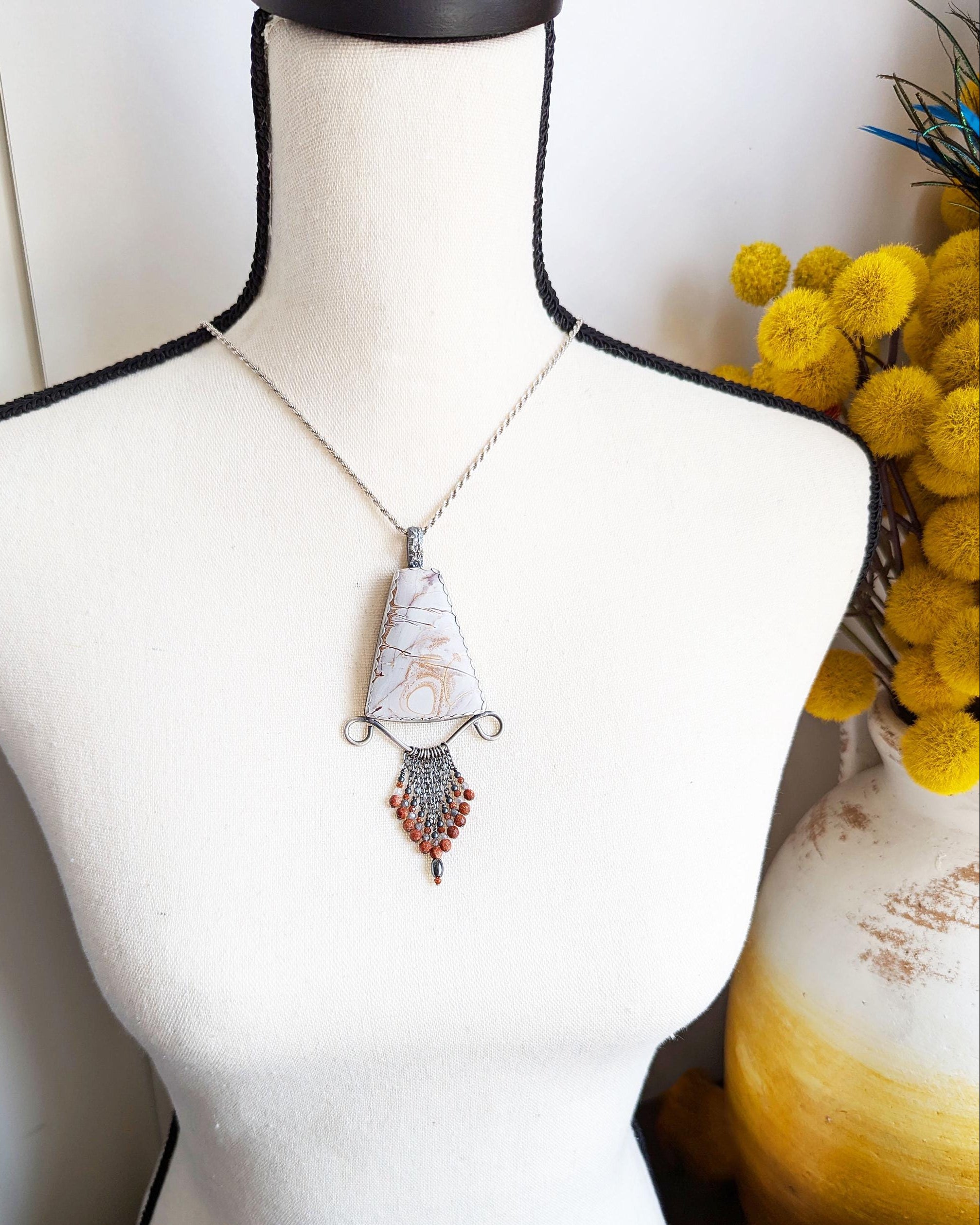 Autumn-inspired artisan pendant in earthy grey and orange tones on bust for scale