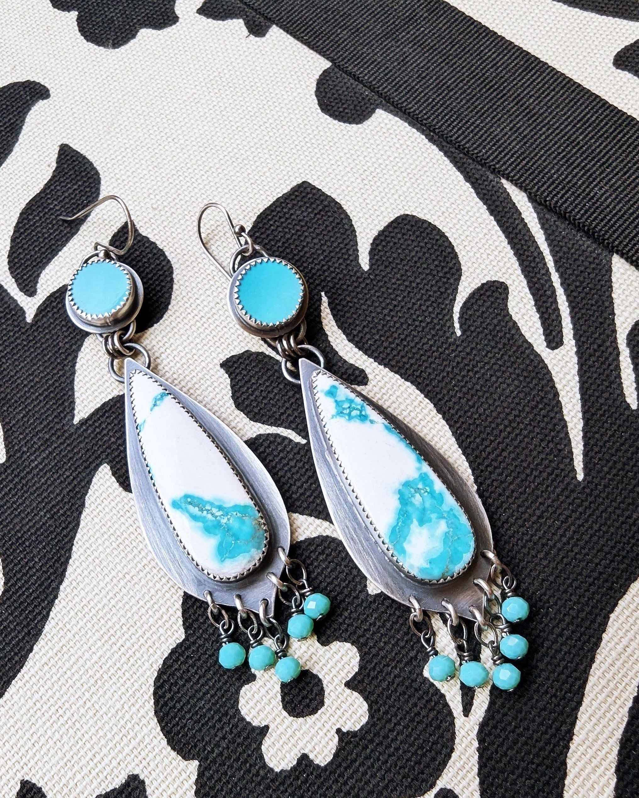 Teardrop-shaped earrings with turquoise stones on a black and white patterned background