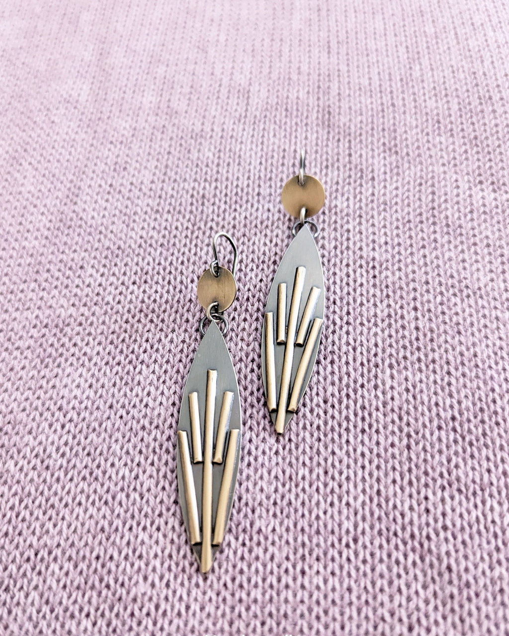 Geometric earrings on a light purple textured fabric background
