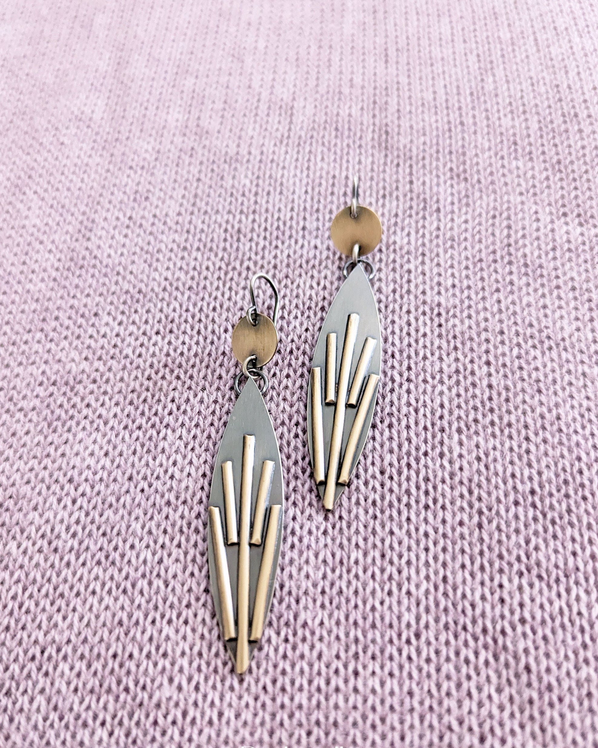 Geometric earrings on a light purple textured fabric background