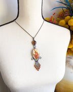 Necklace with a pendant on a mannequin bust, with a blurred background featuring flowers.