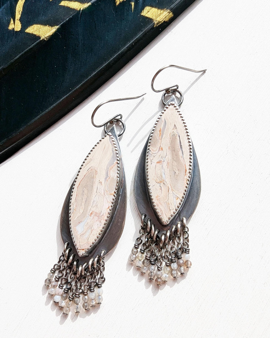 Pair of silver earrings with marquise-shaped stones and dangling beads on a white background.