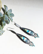 Pair of earrings with a blue and silver design, set against a light background with a plant.