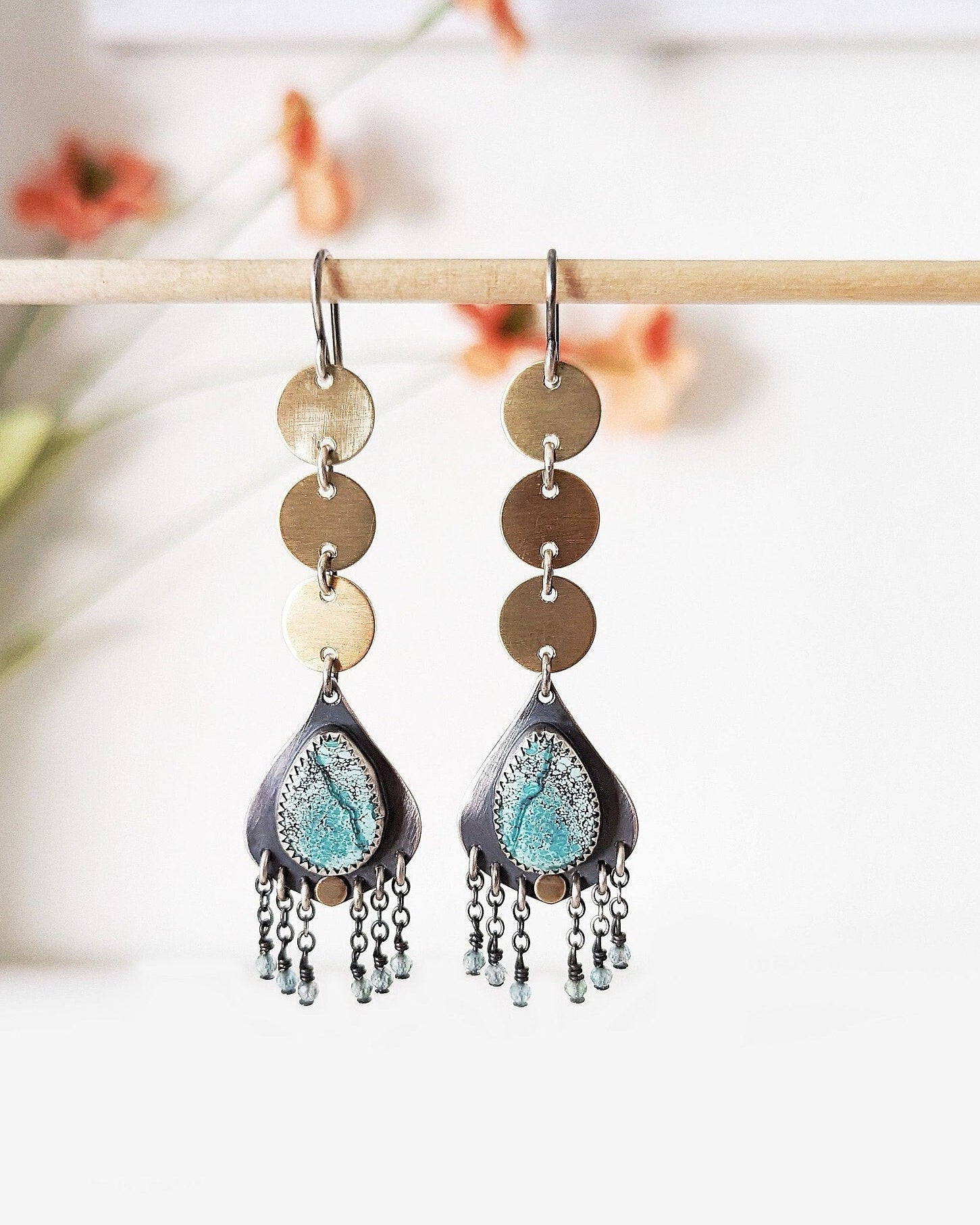 Pair of earrings with 3 circular brass discs that waterfall to a teardrop-shaped turquoise stone with blue bead fringe.