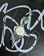 Jewelry set with green and silver elements on a black background with white abstract designs.