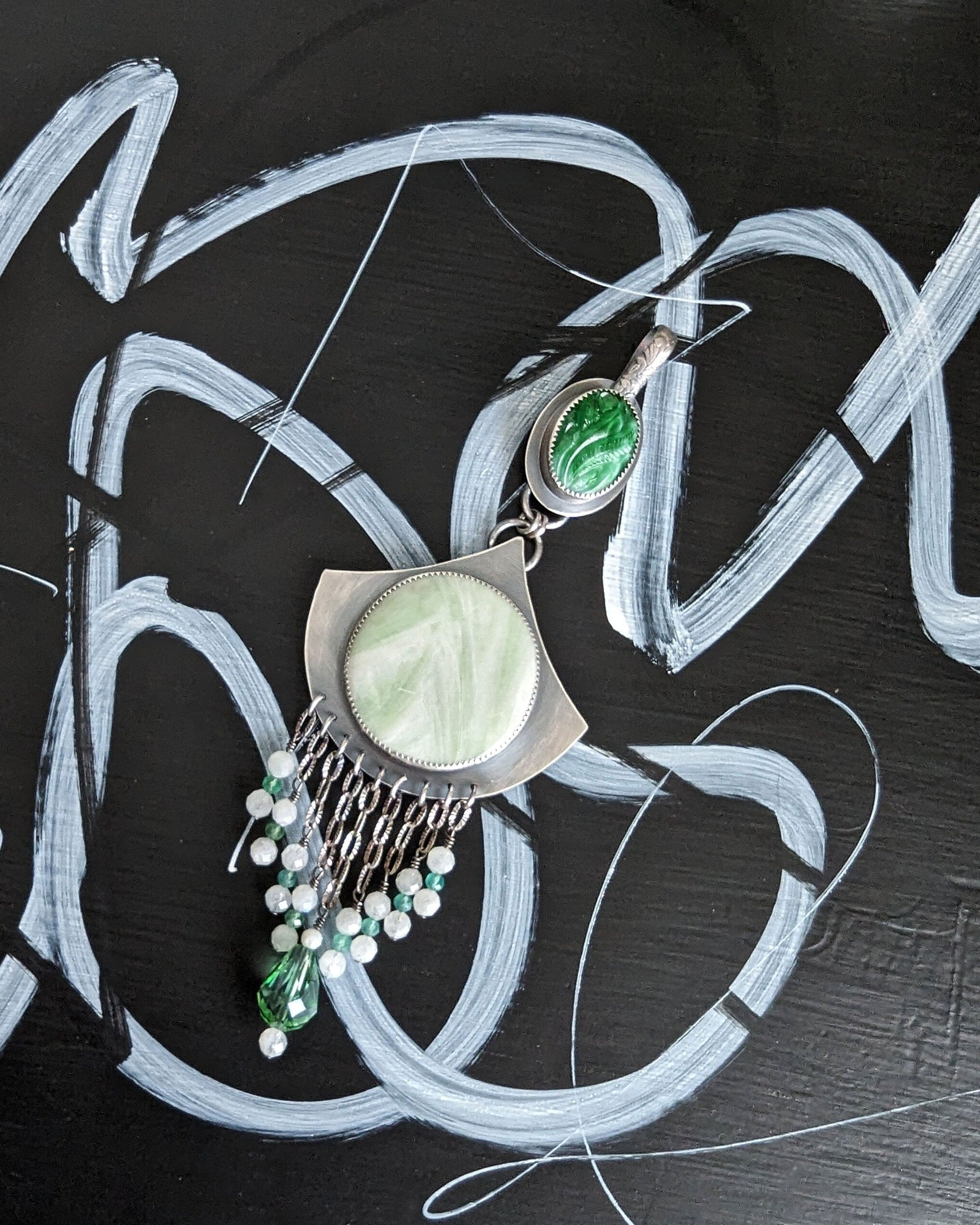 Jewelry set with green and silver elements on a black background with white abstract designs.