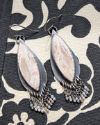 Pair of silver teardrop earrings with chain details on a patterned fabric background