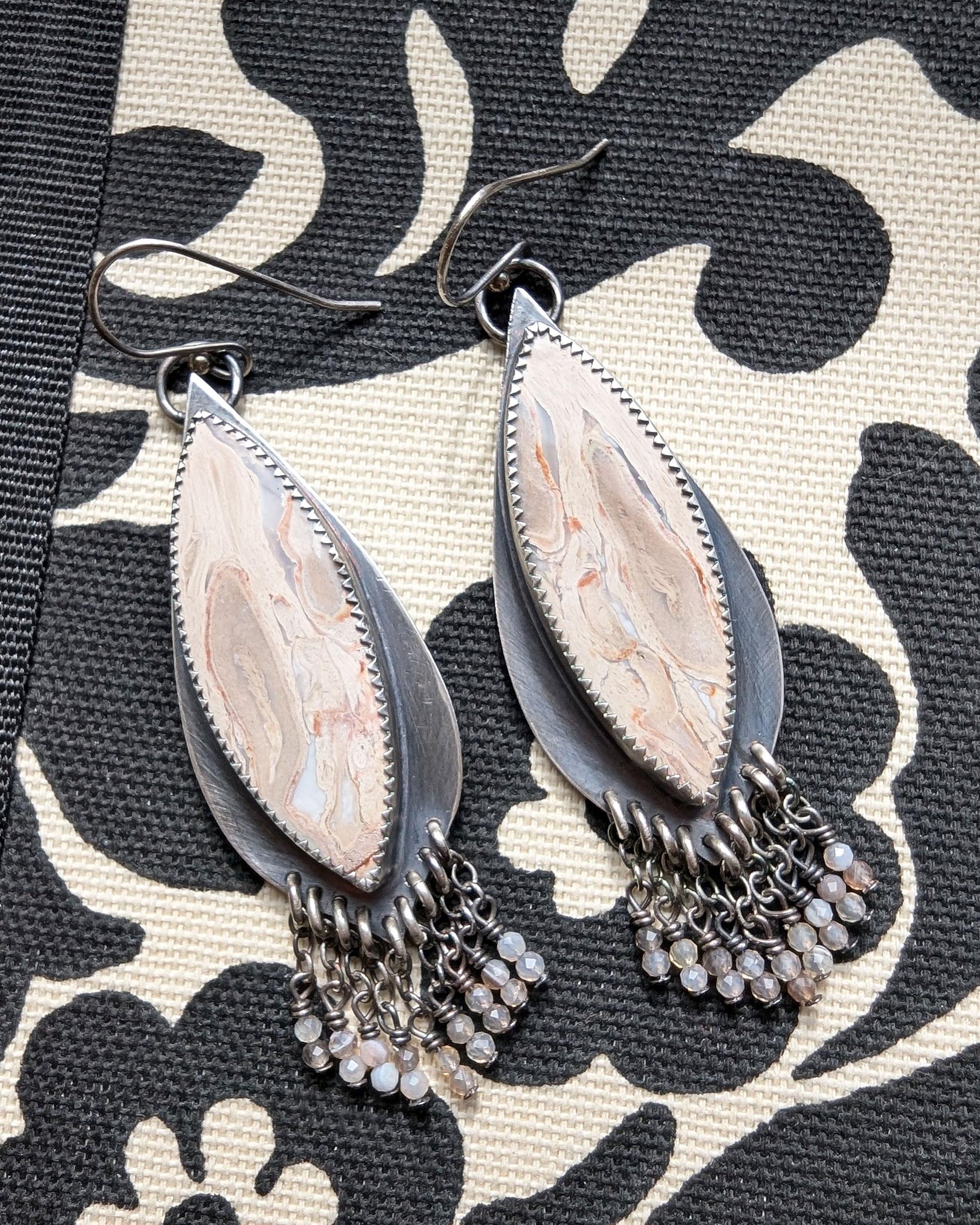 Pair of silver teardrop earrings with chain details on a patterned fabric background