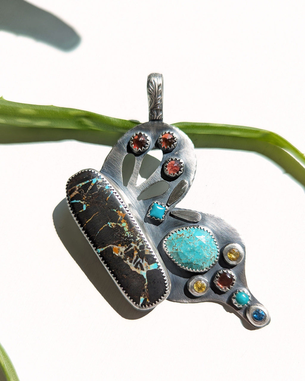 Silver butterfly wing pendant with turquoise and garnets on a white background in bright light