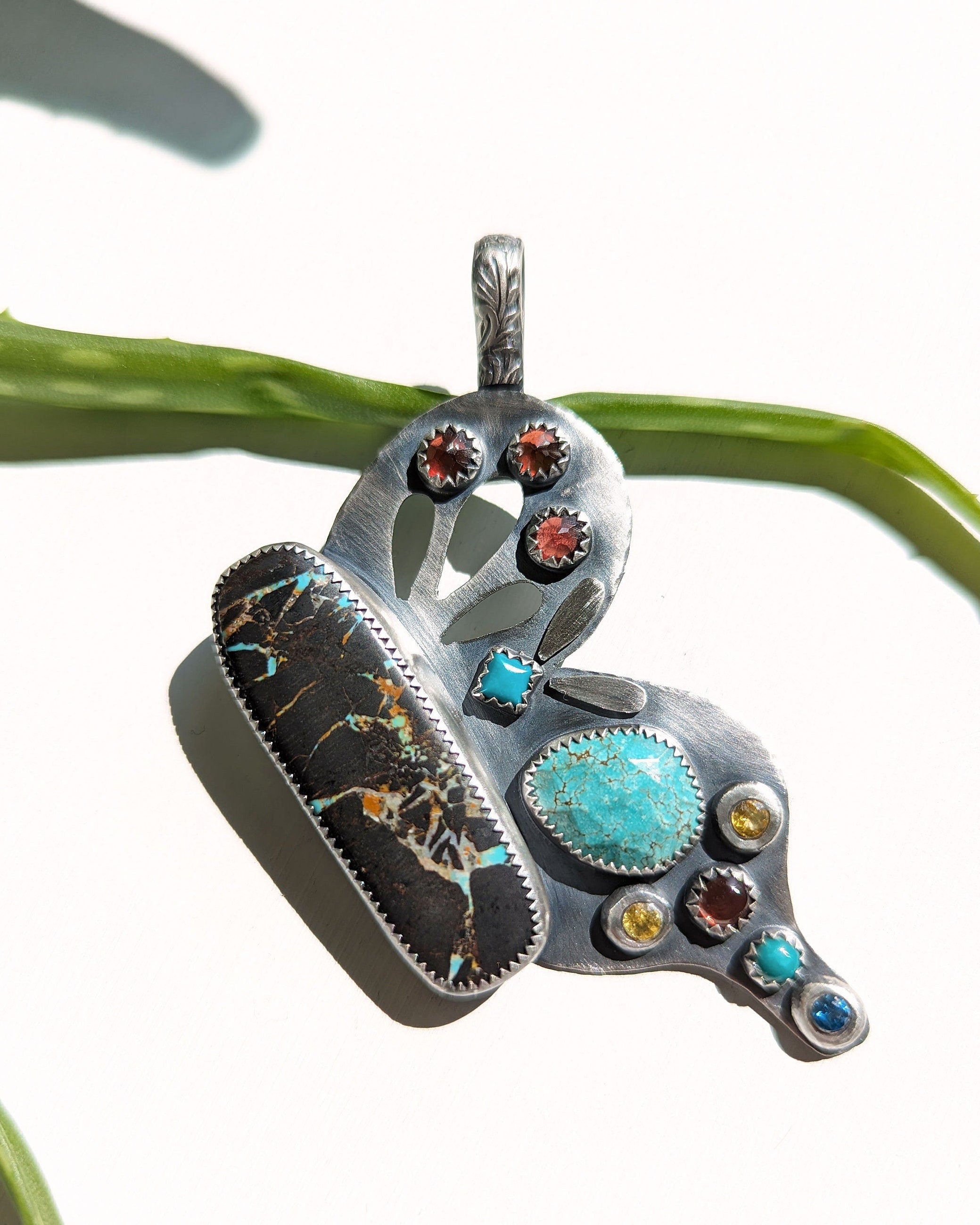 Silver butterfly wing pendant with turquoise and garnets on a white background in bright light
