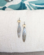 Pair of earrings on a white cushion with a floral-patterned fabric background