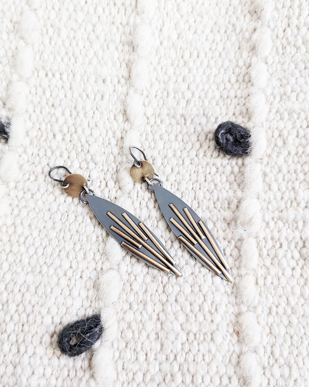 Pair of earrings on a textured white surface with grey looped fabric.