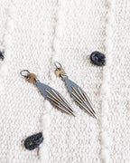 Pair of earrings on a textured white surface with grey looped fabric.