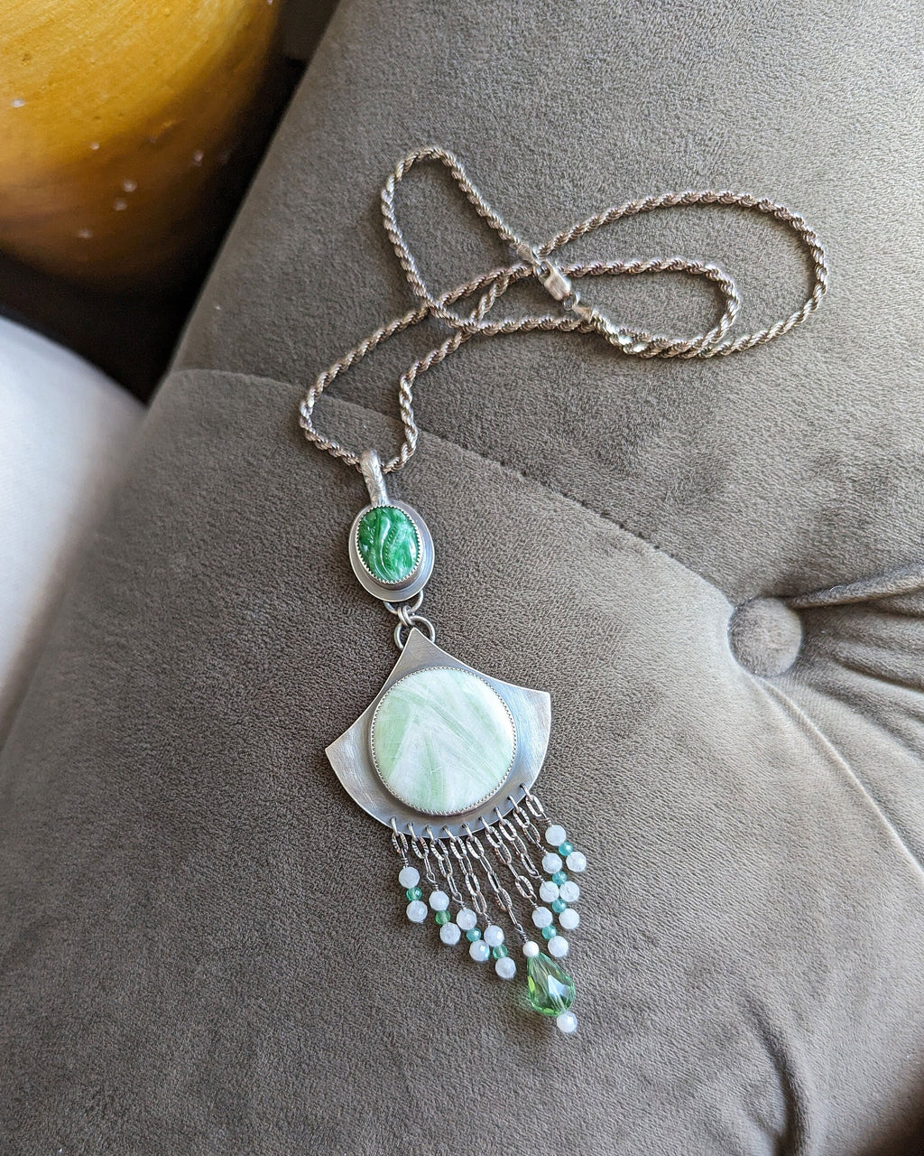Necklace with eye-shaped pendant and green gemstone on a gray cushion