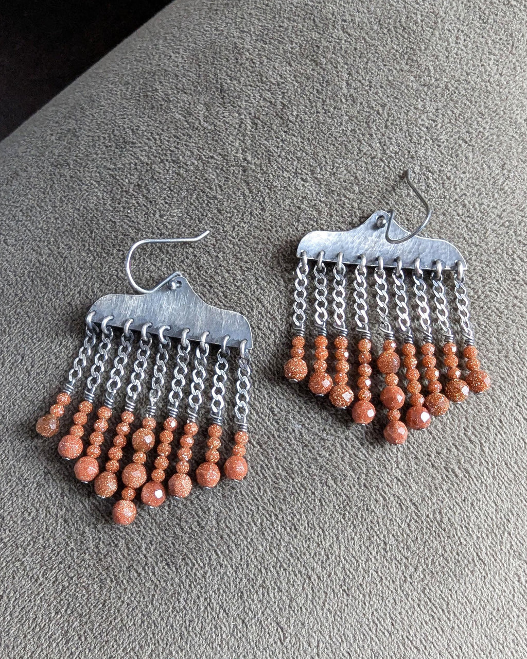Close up of burnt umber orange goldstone bead drops on sterling silver earrings
