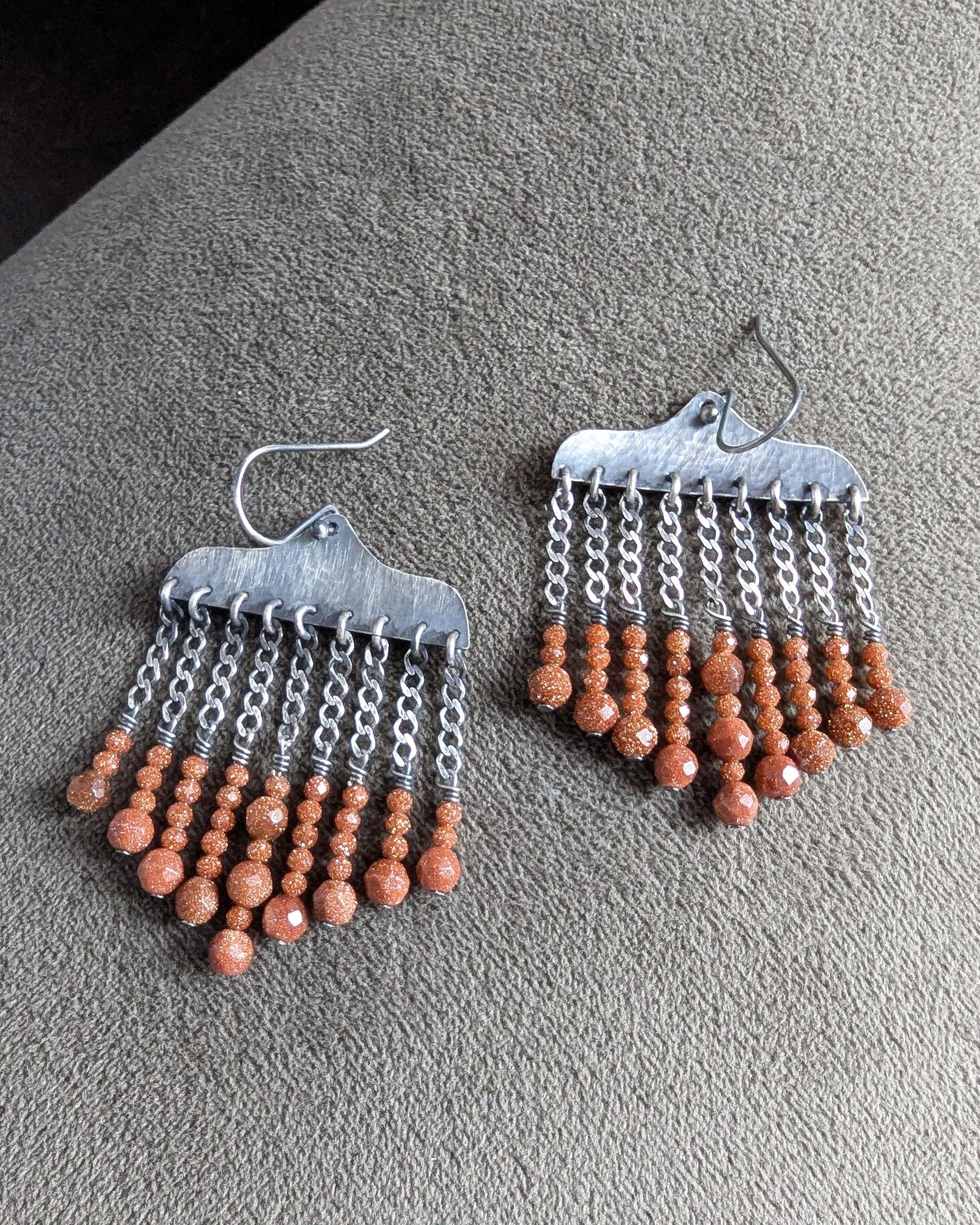 Close up of burnt umber orange goldstone bead drops on sterling silver earrings
