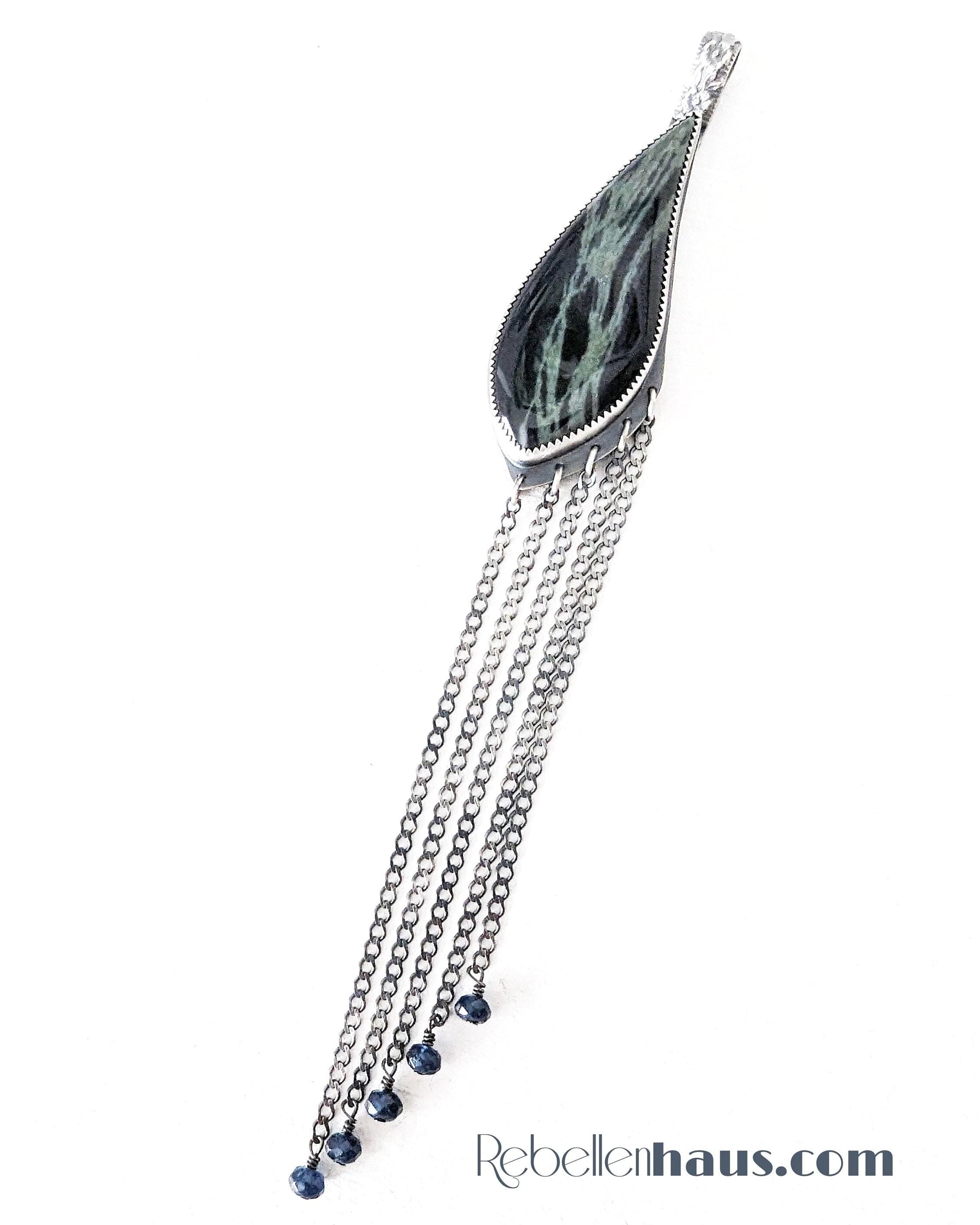 Decorative pendant with chains and a green stone on a white background, featuring the brand 'Rebellenhaus.com'.