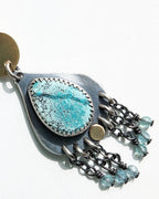 Close up of speckled slightly greenish blue turquoise stone and blue bead fringe on white background.