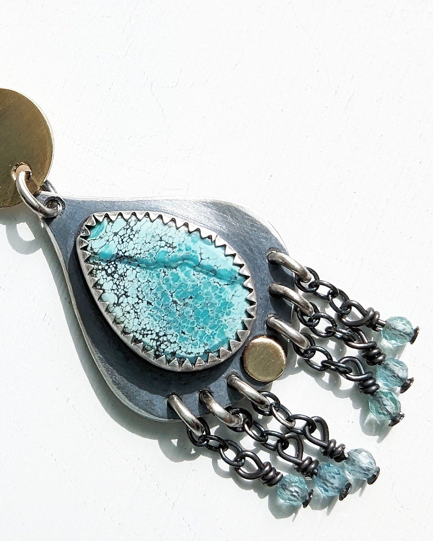 Close up of speckled slightly greenish blue turquoise stone and blue bead fringe on white background.