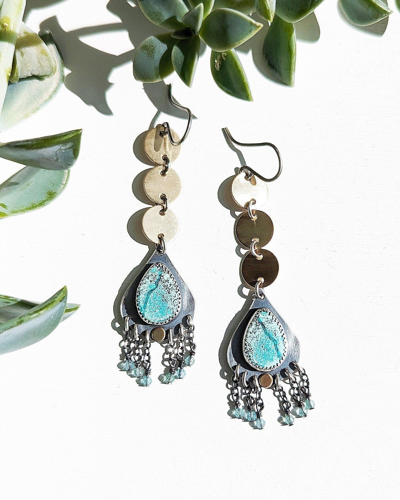 Pair of earrings with 3 circular brass discs that waterfall to a teardrop-shaped turquoise stone with blue bead fringe.