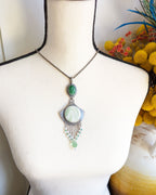 Necklace with green pendant on a mannequin bust with flowers in the background