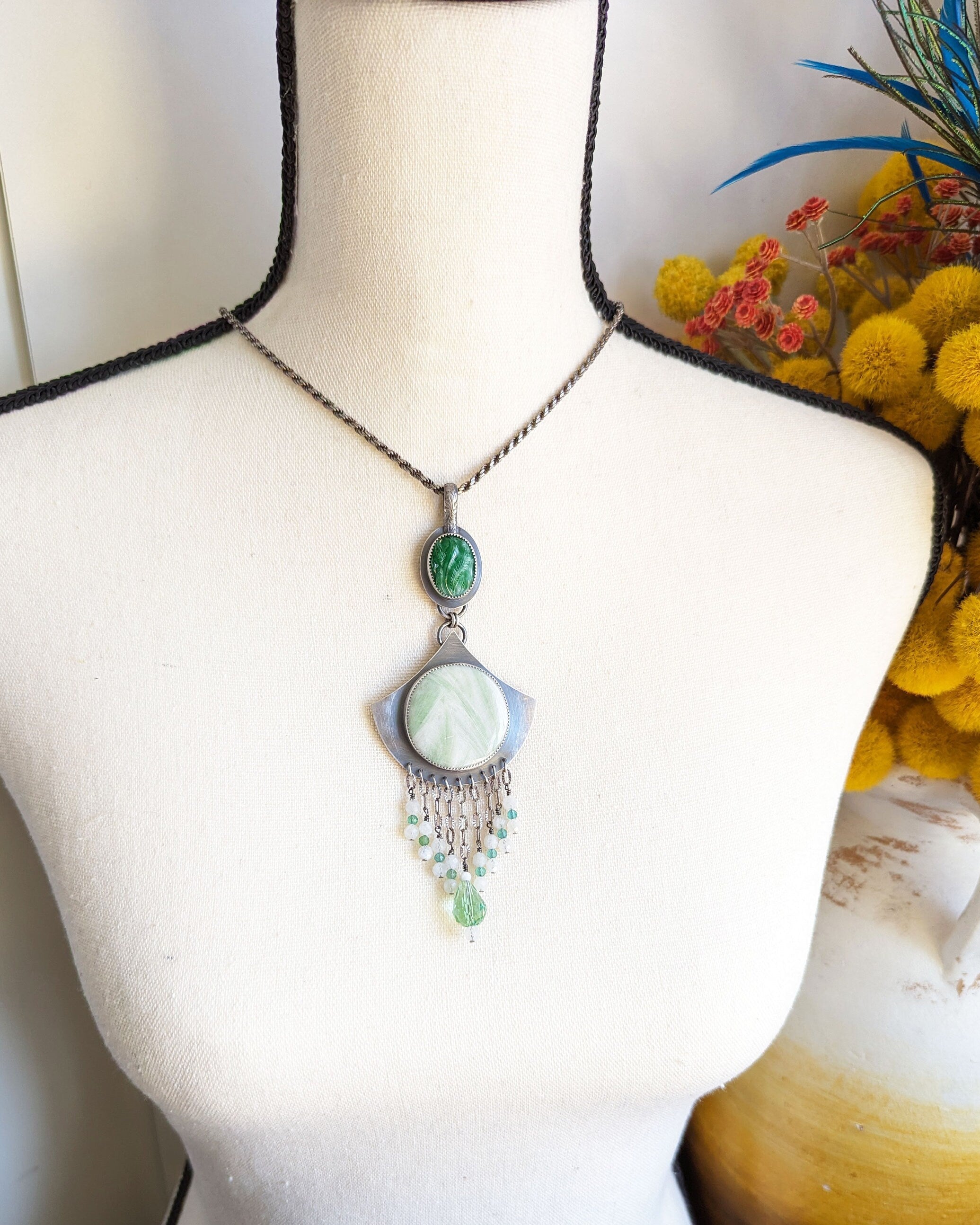 Necklace with green pendant on a mannequin bust with flowers in the background