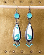 Two stone teardrop-shaped earrings with turquoise and jasper stones hanging in front of gold background