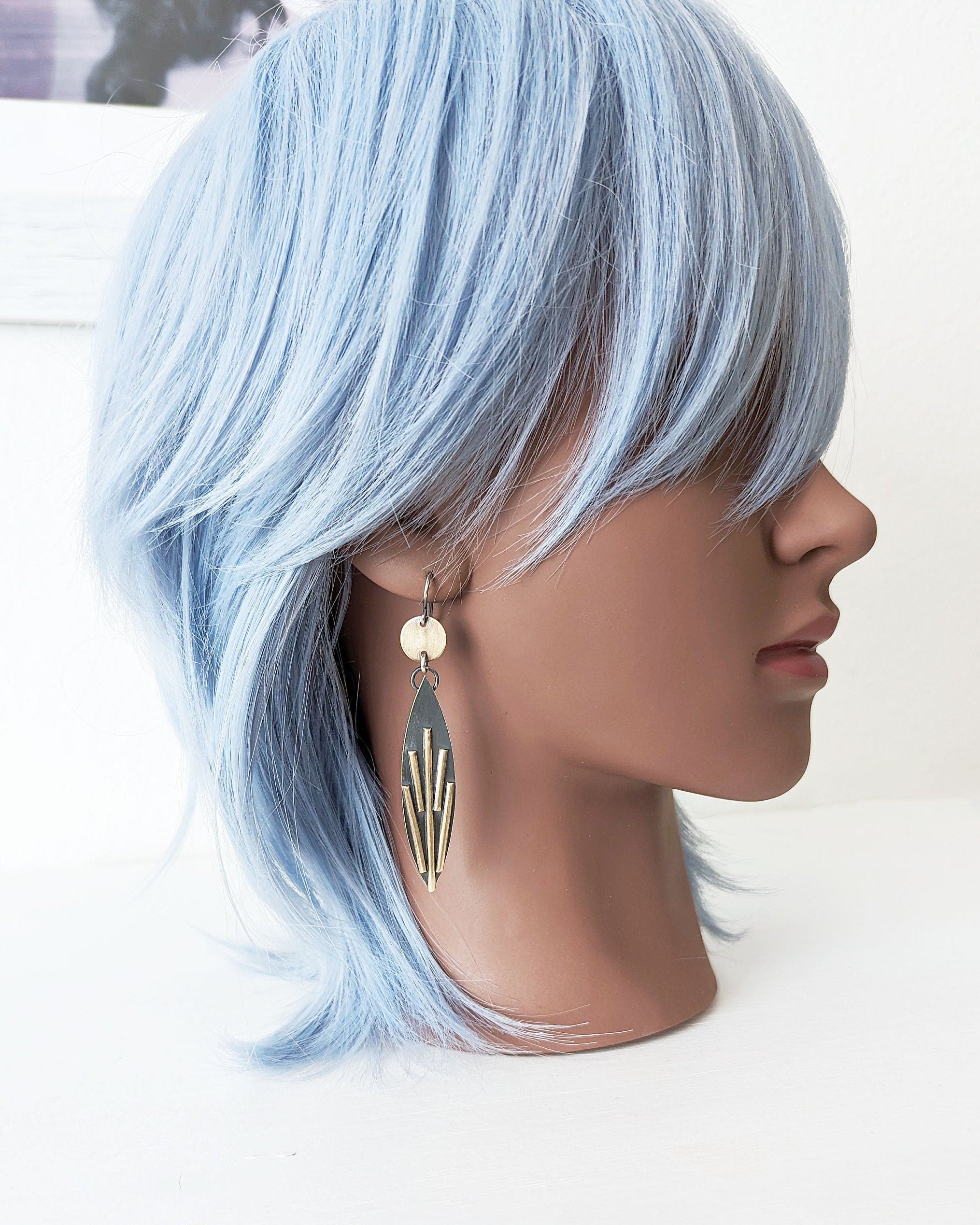 Mannequin head with light blue hair and earrings on a white background.