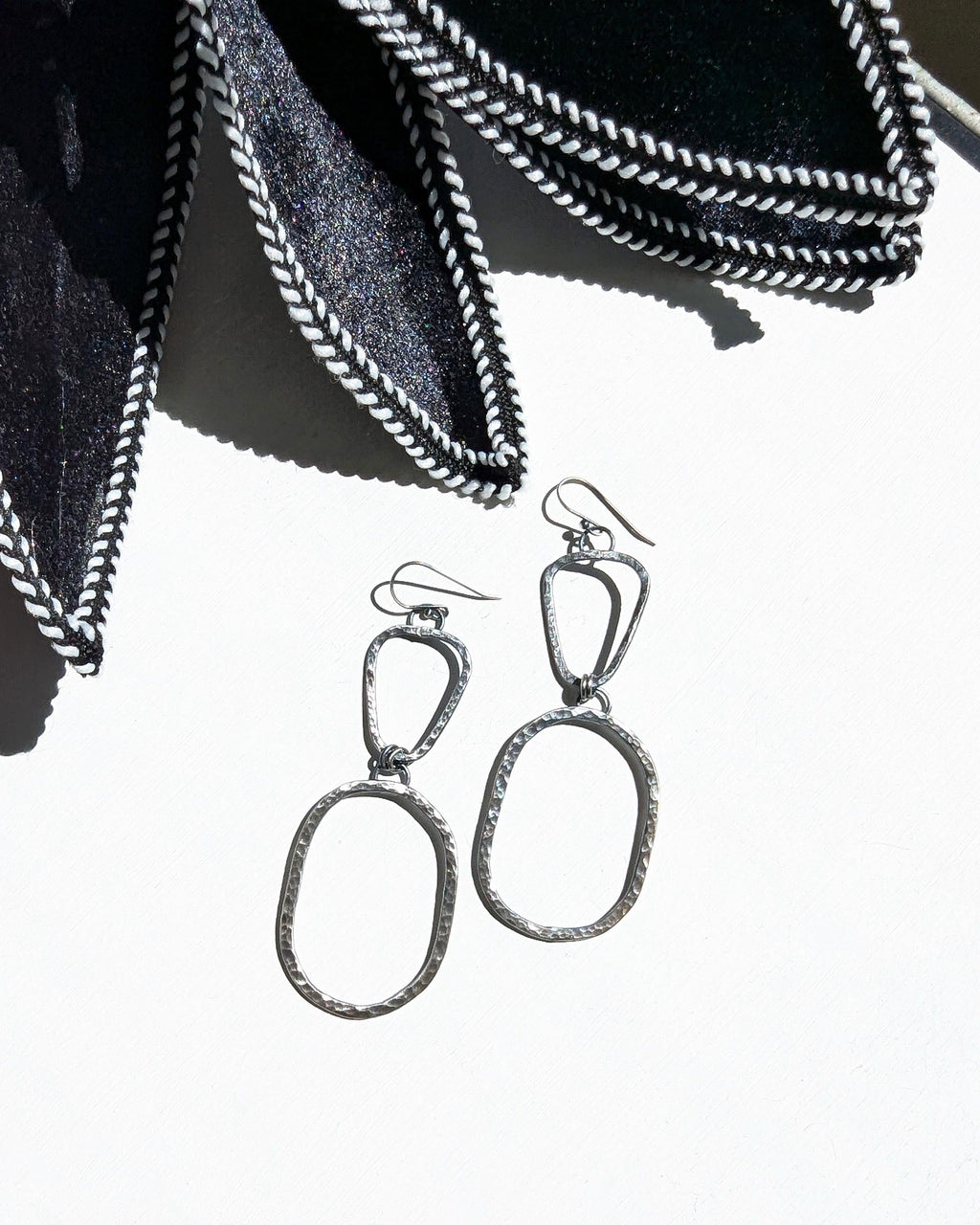 Pair of silver earrings on a white surface with black petals.