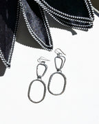 Pair of silver earrings on a white surface with black petals.