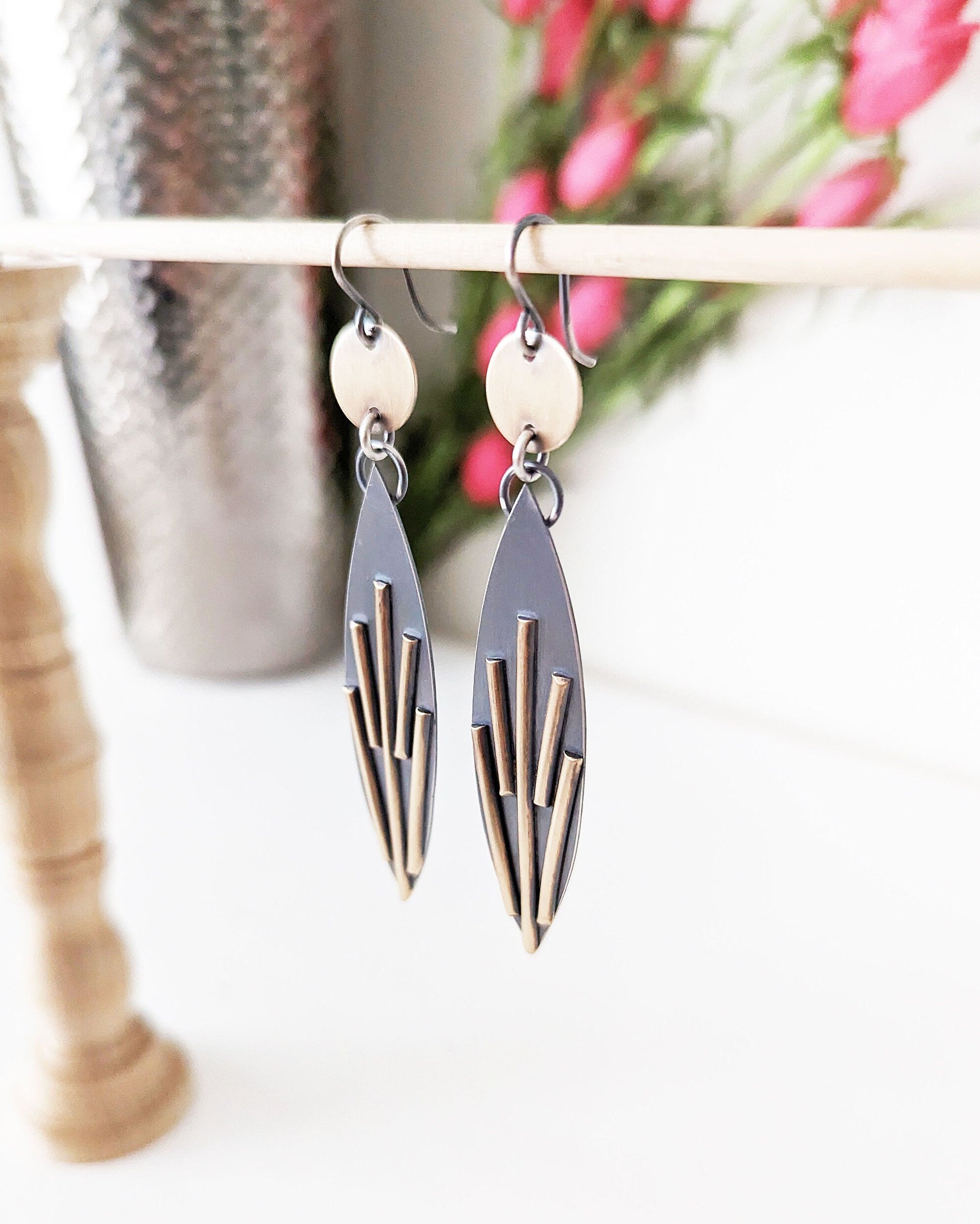 Pair of geometric earrings hanging on a rack with flowers in the background.