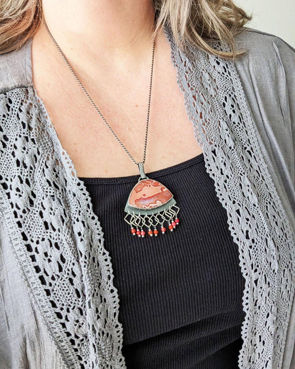 Handcrafted orange agate pendant with fringe and oxidized sterling silver shown on model for scale