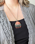 Handcrafted orange agate pendant with fringe and oxidized sterling silver shown on model for scale