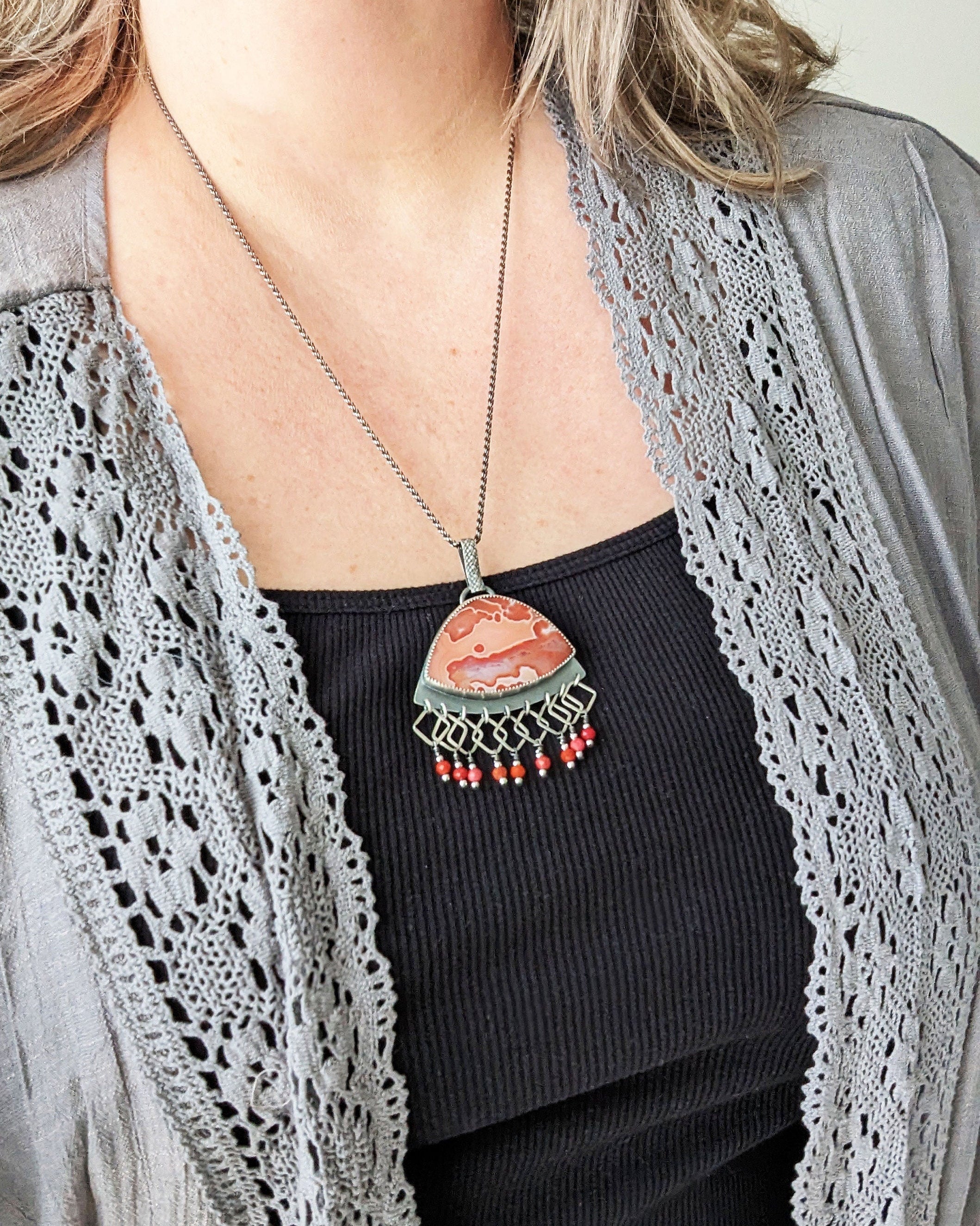 Handcrafted orange agate pendant with fringe and oxidized sterling silver shown on model for scale