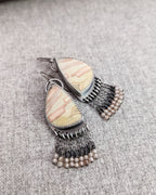 Asymmetrical gemstone earrings featuring pink, cream, and peach banded agate