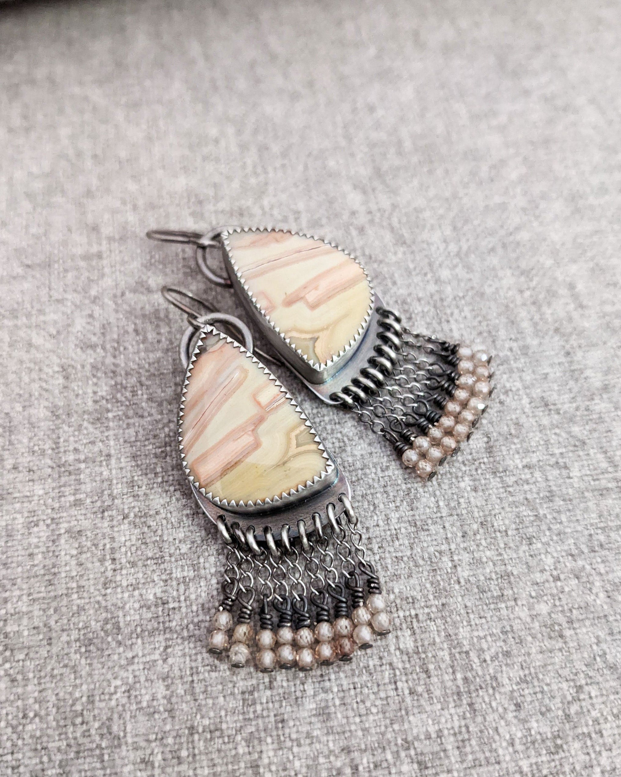 Asymmetrical gemstone earrings featuring pink, cream, and peach banded agate