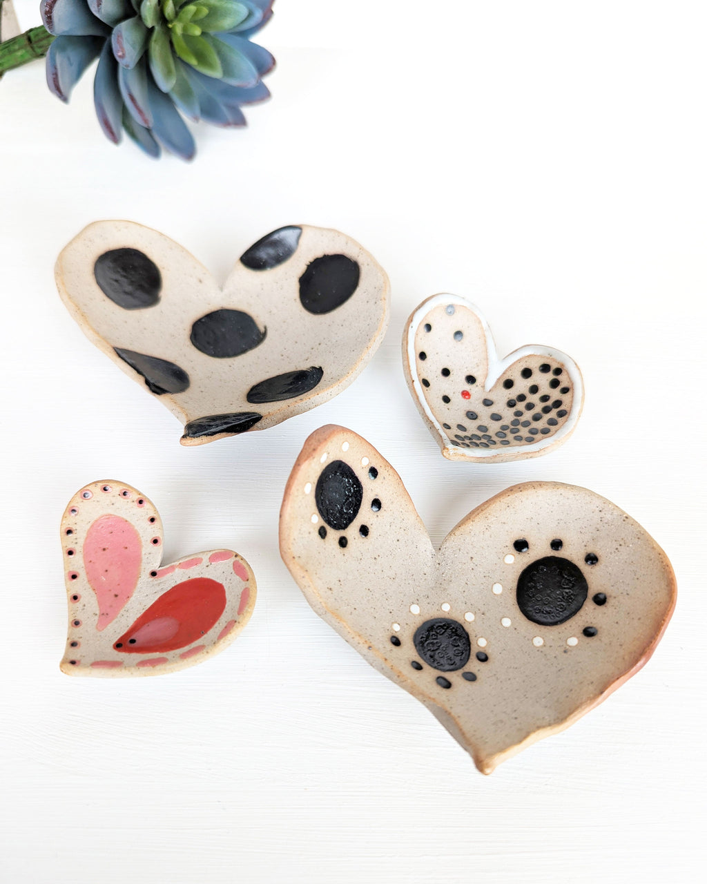 Four handmade ceramic heart dishes with unique painted patterns in rustic stoneware clay.