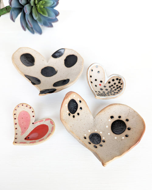 Four handmade ceramic heart dishes with unique painted patterns in rustic stoneware clay.
