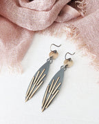 Pair of earrings with geometric design on a light pink fabric background.