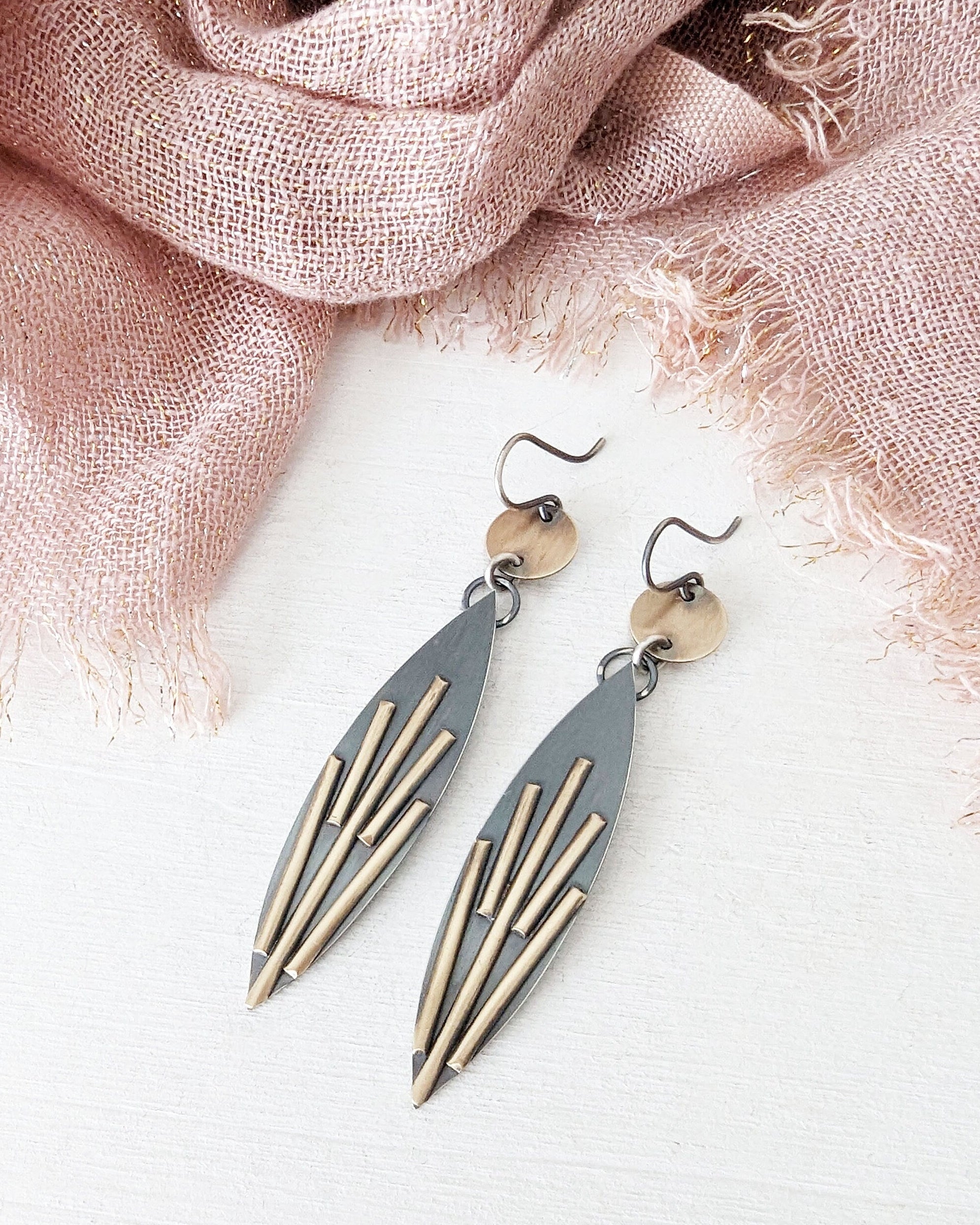 Pair of earrings with geometric design on a light pink fabric background.
