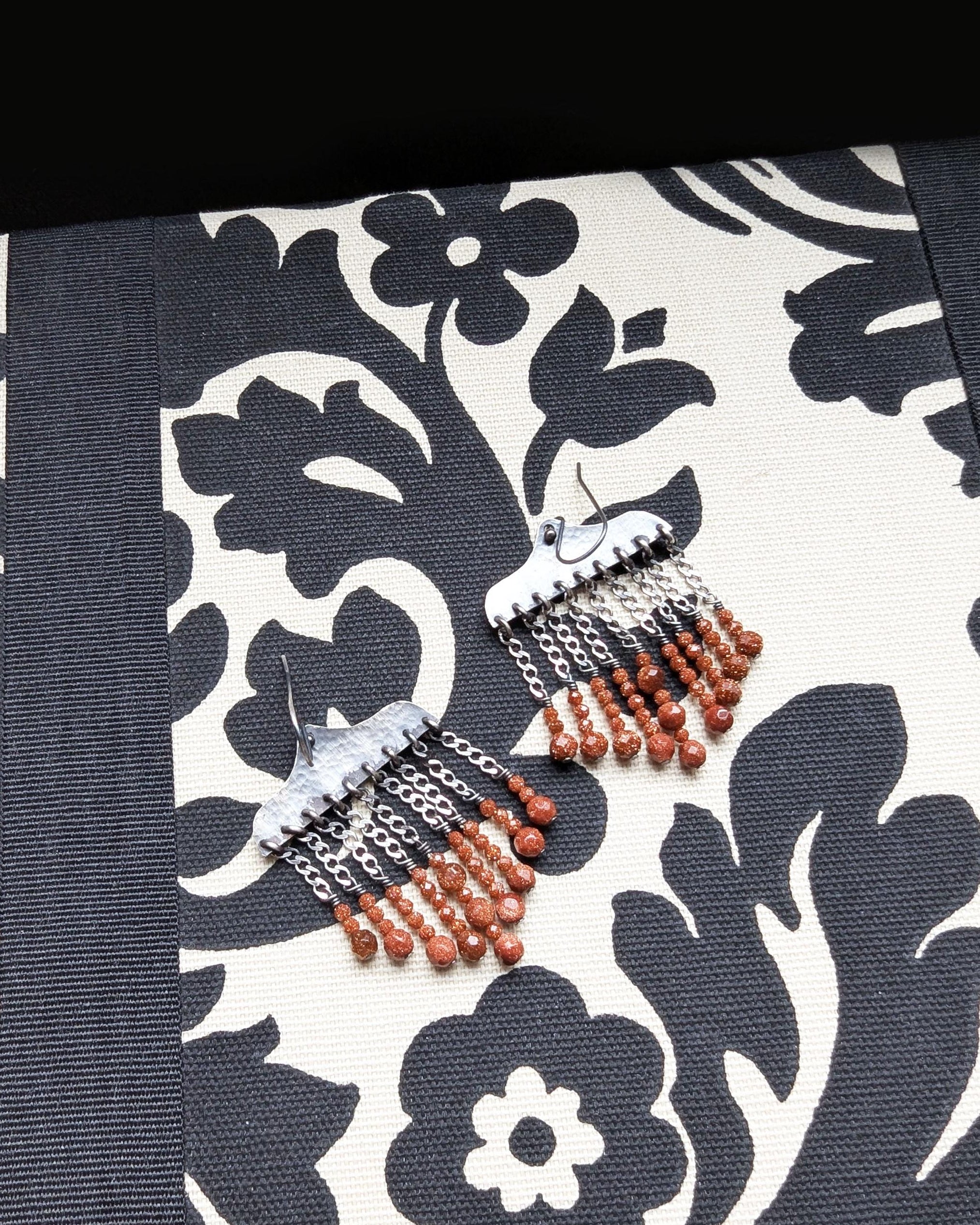 Orange goldstone earrings with hammered oxidized sterling silver and bead drops on fabric background

