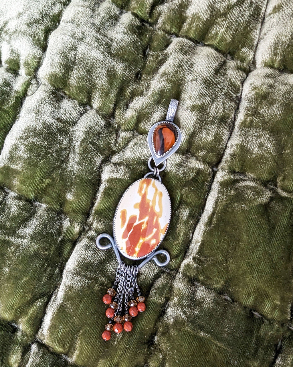 Jewelry pendant with a stone and beads on a textured green fabric background